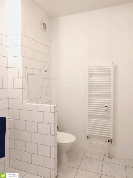 A bathroom in a studio apartment with white tiles and a towel rack.