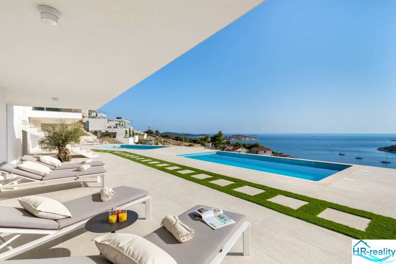 Terrace area with sunbeds, a swimming pool, and a sea view in a holiday apartment in Rogoznica.