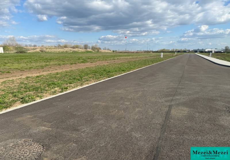 An asphalt road leading between green commercial properties in Trnava under a cloudy sky.