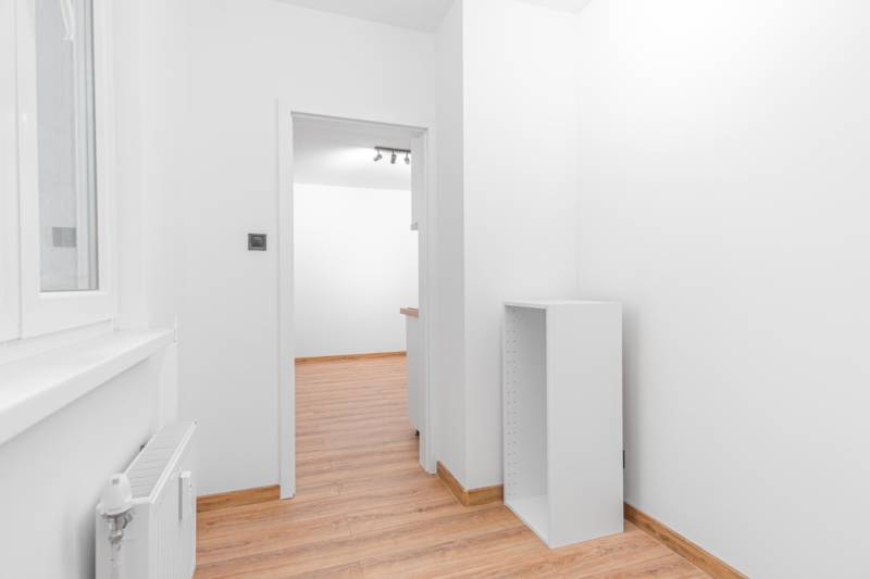 A bright room in a one-bedroom apartment with wood-patterned flooring and white walls.