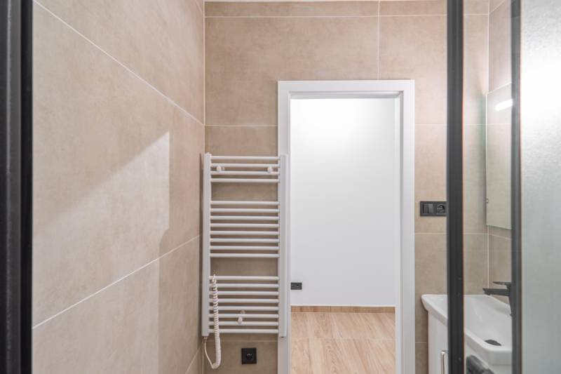 A bathroom with light tiles and a ladder radiator in a studio apartment.