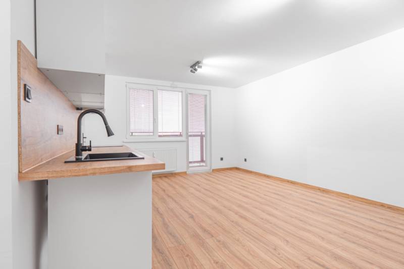 Living room in a studio apartment with a wood-patterned floor and built-in kitchen unit.