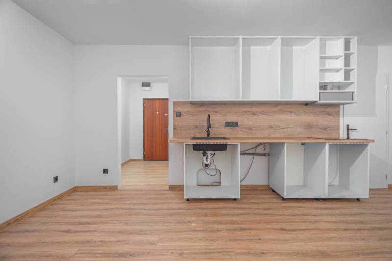 An empty kitchen unit with wood-decor flooring in a studio apartment.