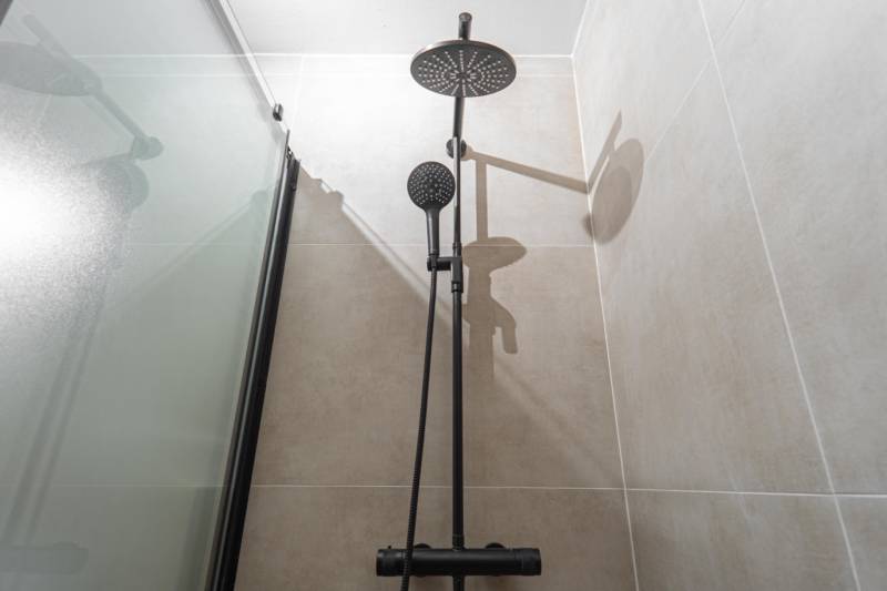 Shower head and square bathtub in the bathroom of a studio apartment.