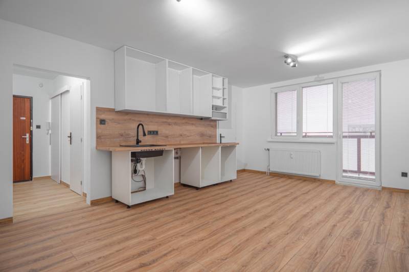 Kitchen unit in a studio apartment with white cabinets and a wood-patterned floor.