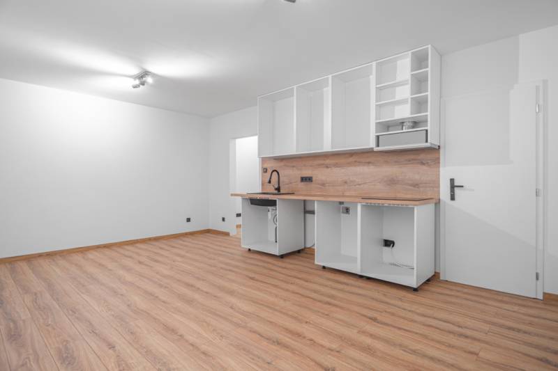 A kitchen in a studio apartment with a wood-patterned floor and white cabinets.