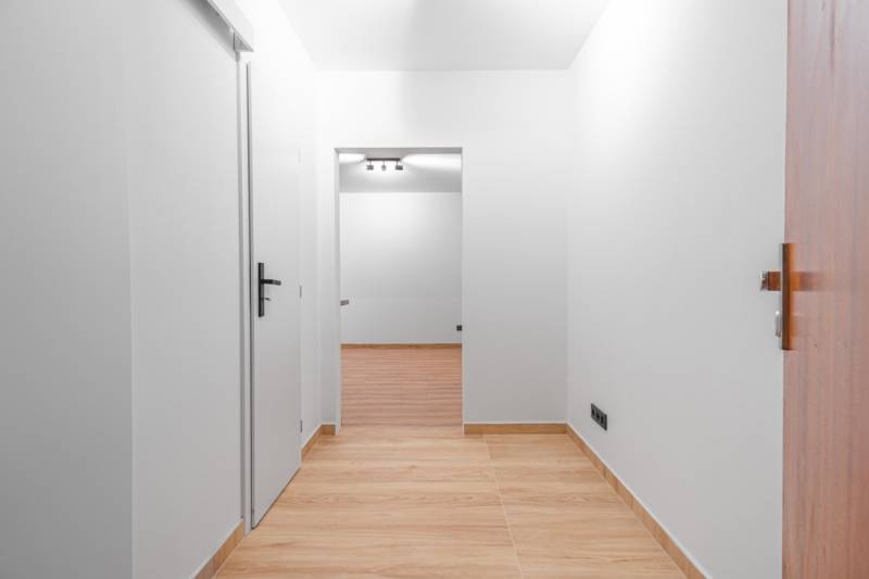 A bright white hallway with a wood-patterned floor in a studio apartment.