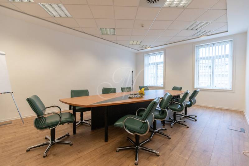 Conference room with an oval table, green chairs, and a wood-patterned floor.