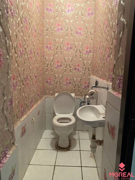 A toilet with pink floral wallpaper and white tiles in a family house.