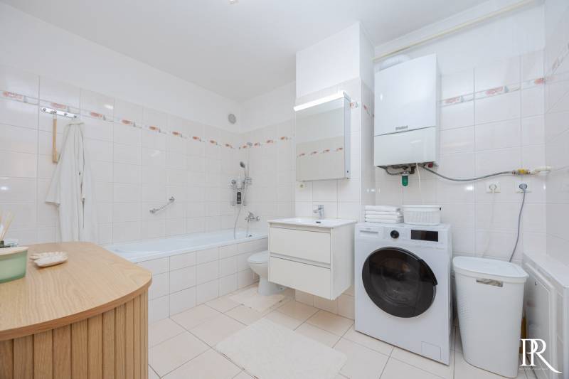 Bathroom in a 2-room apartment with a bathtub, washing machine, and light tiles.