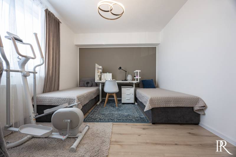 A bedroom in a 2-room apartment with two beds, a desk, and an exercise bike.