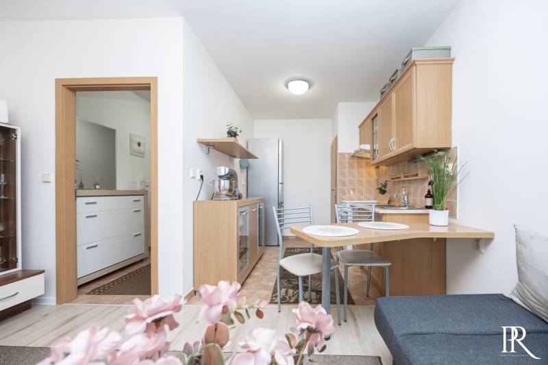A kitchen in a 2-room apartment with a dining table, light cabinets, and flowers on the table.