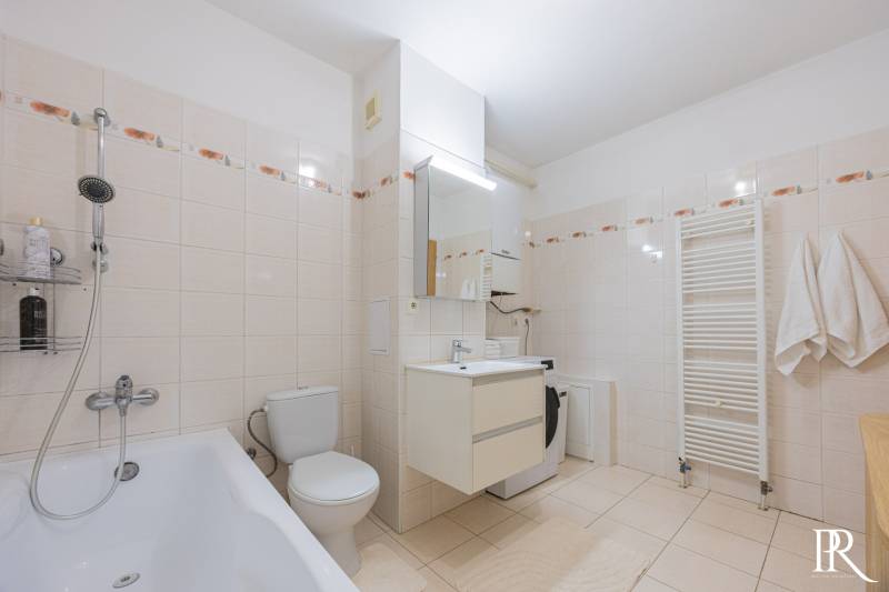 Bathroom with a bathtub, sink, and washing machine in a 2-room apartment. Flat tiles with a floral pattern.