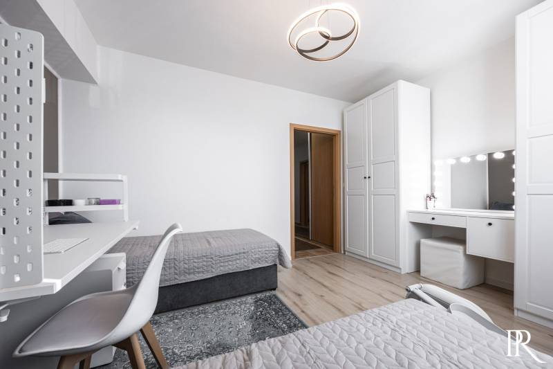A bedroom in a two-room apartment with white furniture, wooden decor flooring.