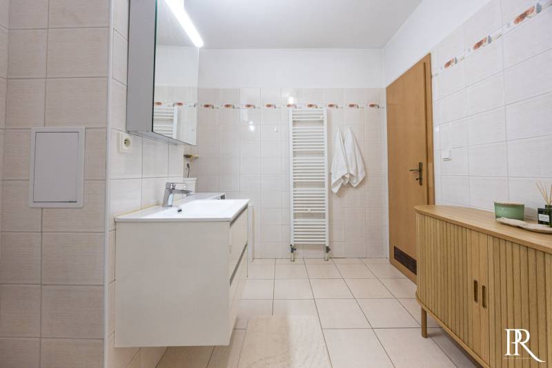 A bathroom in a 2-room apartment with a white washbasin cabinet and a wooden chest of drawers.