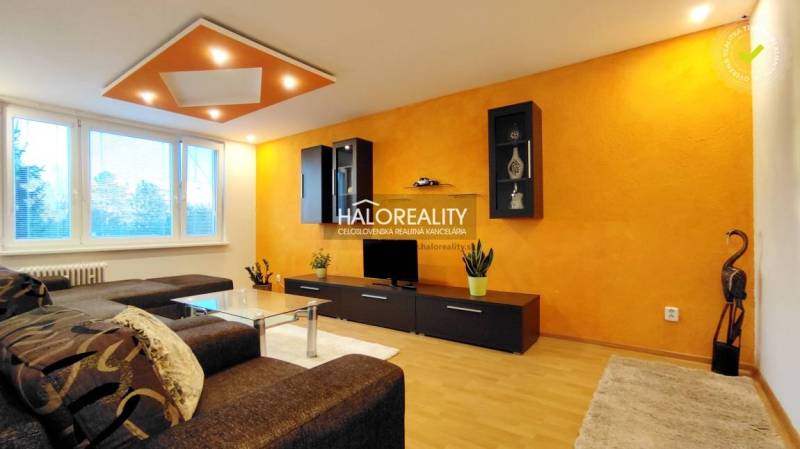 The living room in the two-room apartment has an orange wall and a comfortable brown sofa set.