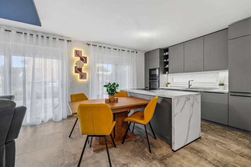 A kitchen in a family house with a dining table, yellow chairs, and a gray kitchen unit.