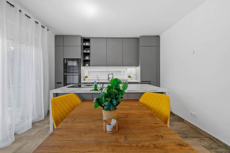 A family house kitchen with a dining table, yellow chairs, and a wooden decor floor.