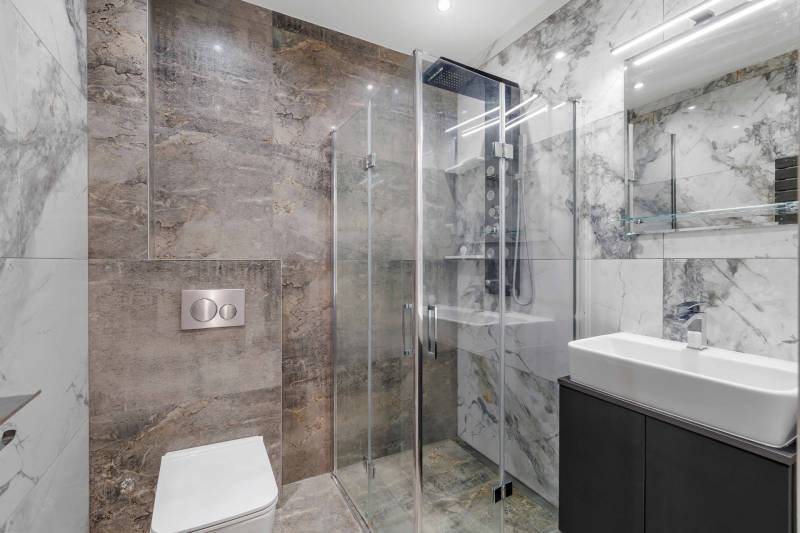 Bathroom with stone cladding, shower enclosure, and sink in a family house.