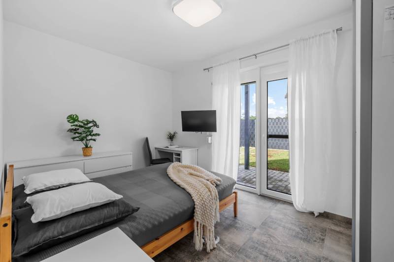 A bedroom in a family house with a bed, a television, and patio doors.