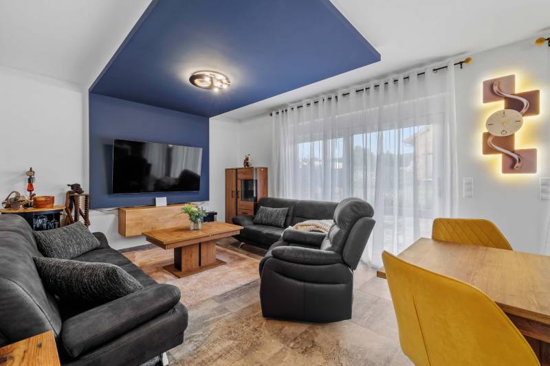 Living room with a black sofa, blue ceiling, and wood-patterned floor in a family house.