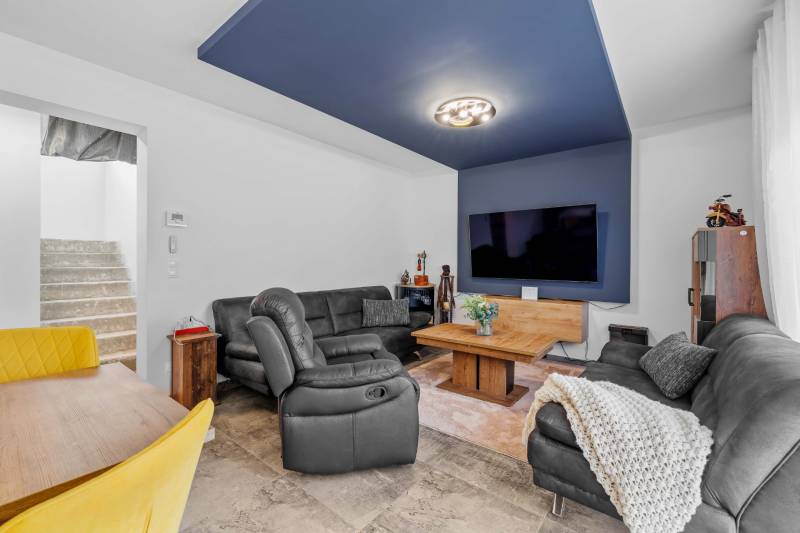 Living room in a family house with a wooden decor floor, leather seating, and a large TV.
