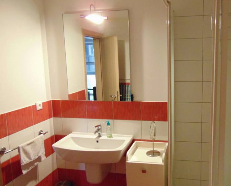 Bathroom in a studio apartment with a sink, mirror, and red and white tiles.