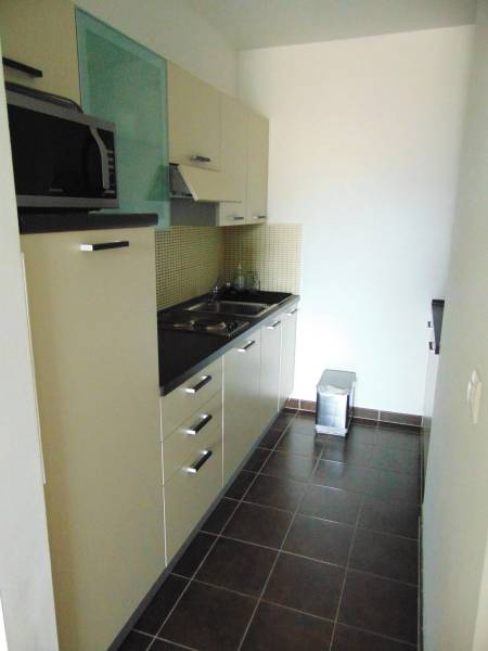 A kitchen in a studio apartment with dark tiles, cabinets, and a microwave.