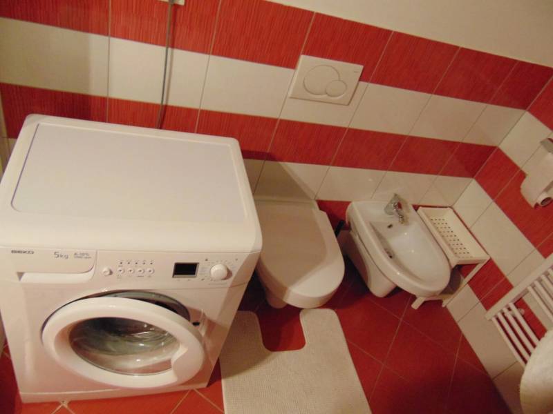 A bathroom with a washing machine, bidet, and red tiles in a studio apartment.