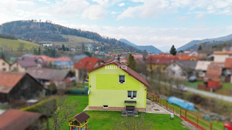 A family house in Kysucké Nové Mesto surrounded by a garden and mountains in the background.