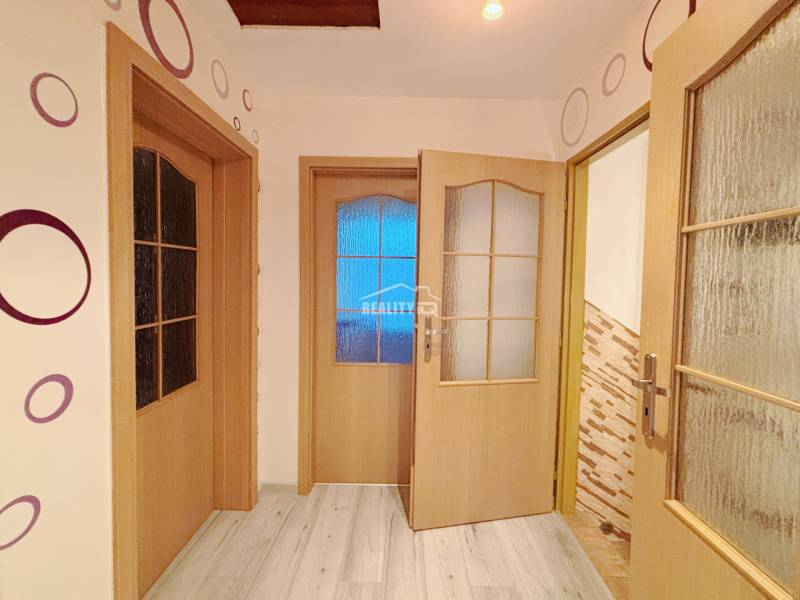 Interior of a family house with patterned wallpaper, wood-effect flooring, and glass doors.