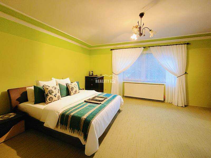 A bedroom in a family house with a bed, green walls, and white curtains.