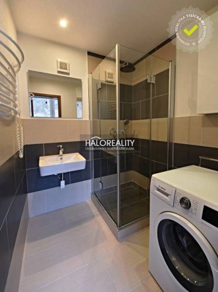 Bathroom in a 2-room apartment with a shower and a washing machine, floor with wood decor.