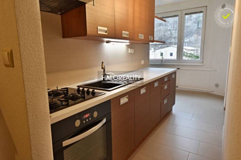 A kitchen in a 2-room apartment with a cooktop, oven, and a window with a view.
