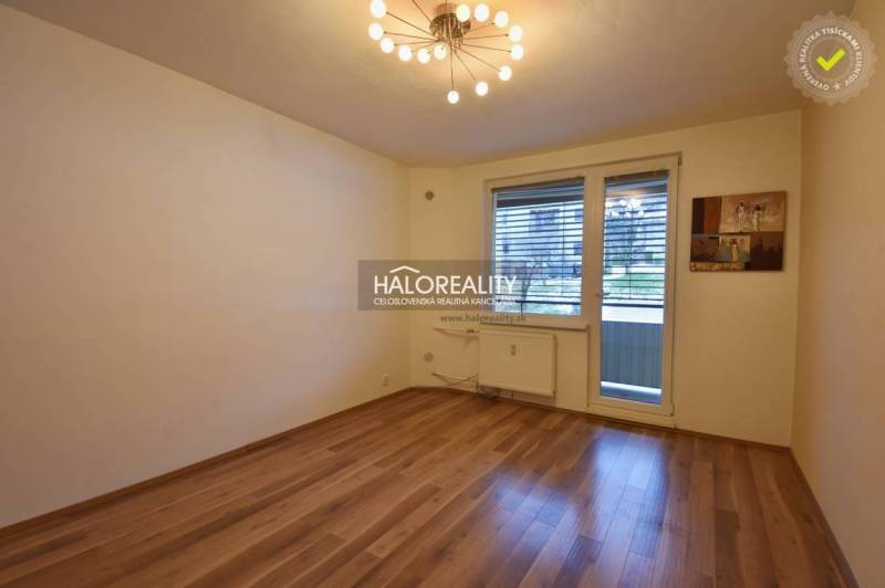 A room in a 2-room apartment with a wooden decor floor and balcony doors.