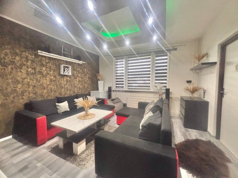 Living room in a 3-room apartment with a wooden decor floor, a black sofa, and decorations.