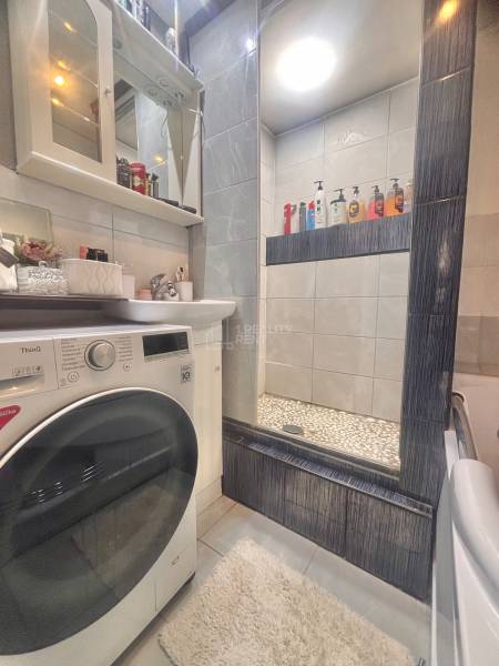 A bathroom in a 3-room apartment with a shower, sink, and washing machine with modern equipment.