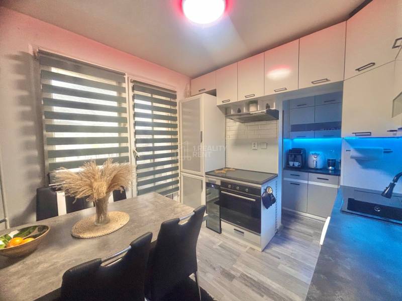 A kitchen in a 3-room apartment with a modern kitchen unit, table, and floor with a wooden decor.