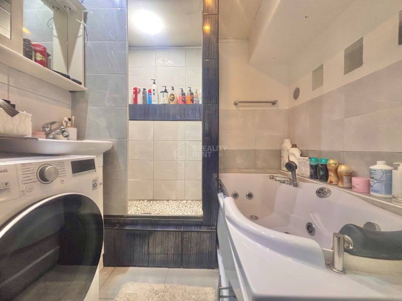 A bathroom with a washing machine, sink, and whirlpool bathtub in a 3-room apartment.