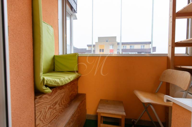 Glazed balcony in a 1-room apartment with wooden seating and light furniture.