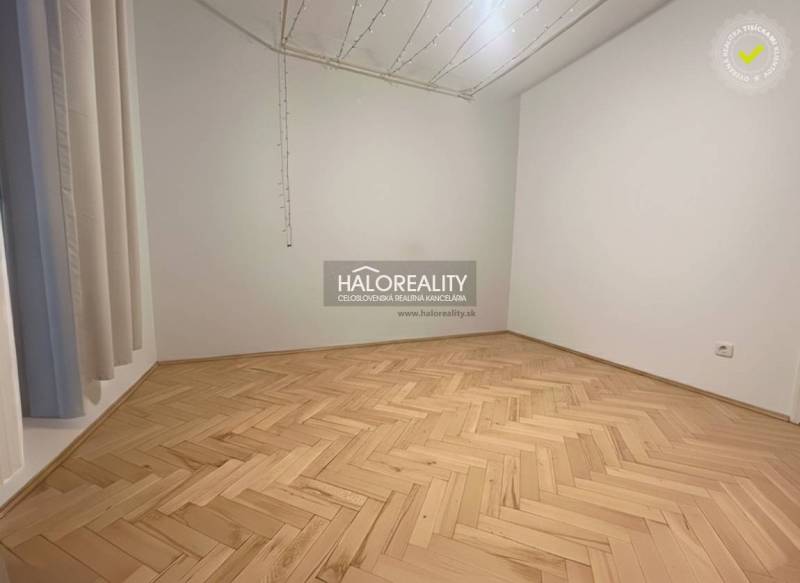 An empty room of a three-room apartment with a wood-patterned floor and pendant lights.