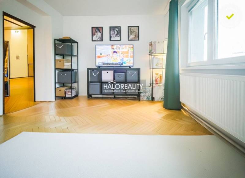 Living room of a three-room apartment with a light wood-patterned floor and a television.
