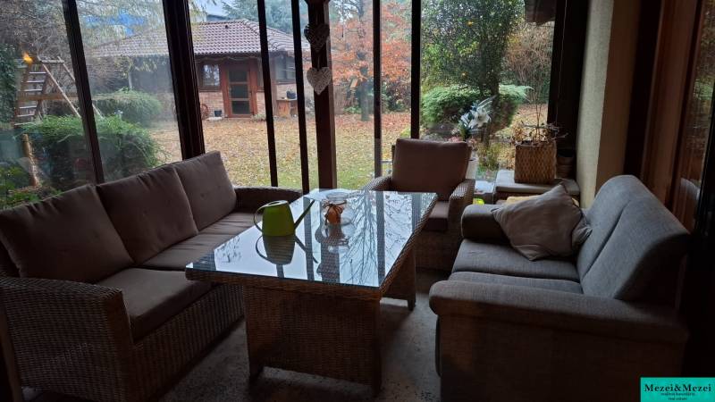 A glazed terrace of a family house with comfortable seating and a view of the garden.