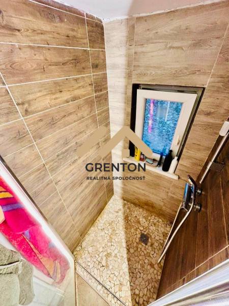 A shower corner with wood decor in a cottage interior, complemented by mosaic tiles and a window.