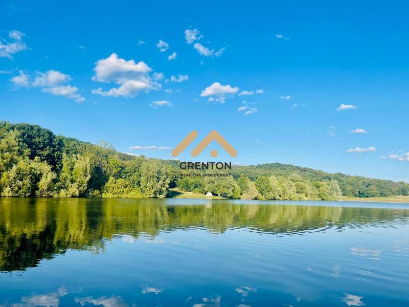 A lake in a wooded landscape with a blue sky near Kučišdorská Valley in Pezinok.