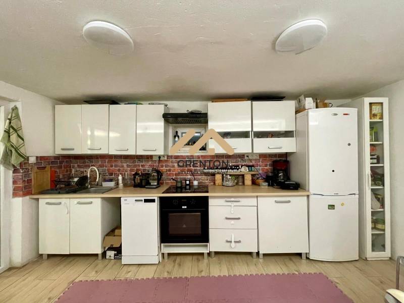 A kitchen in a cottage with white cabinets, brick cladding, and wood-patterned flooring.