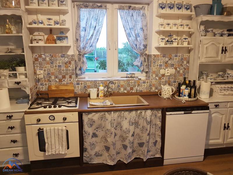 A kitchen in a family house with a country style, patterned tiles, blue curtains.