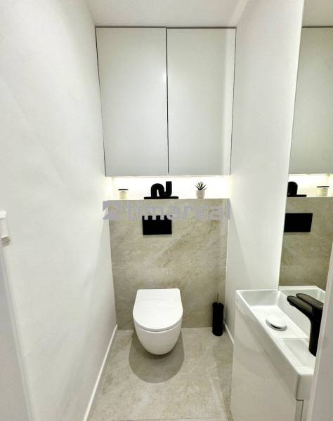 Bathroom in a 4-room apartment with a simple sink and wall-mounted toilet, light tiles.