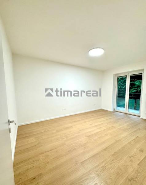 A room in a 4-room apartment with a wood-patterned floor and a large window.