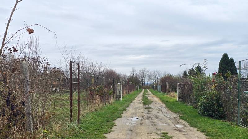 The rural road in Drahovce leading through the Recreational plots, lined with fences and vegetation.